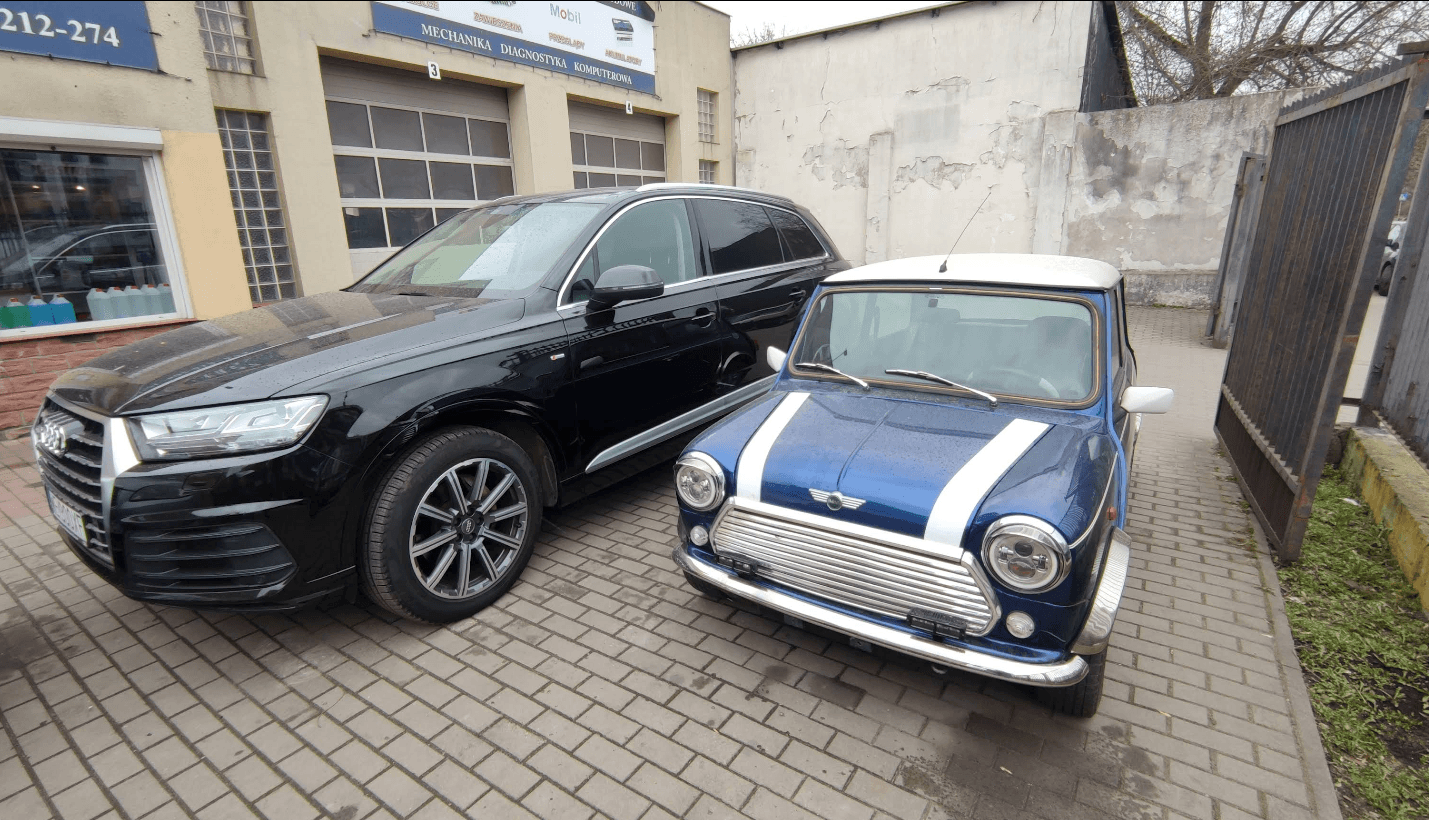 Czarne Audi Q7 zaparkowane obok klasycznego niebieskiego Mini Coopera przed warsztatem Auto-Serwis na Mińskiej.